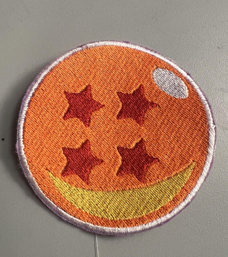 An embroidered patch of the four star dragon ball. It is orange, with four red stars