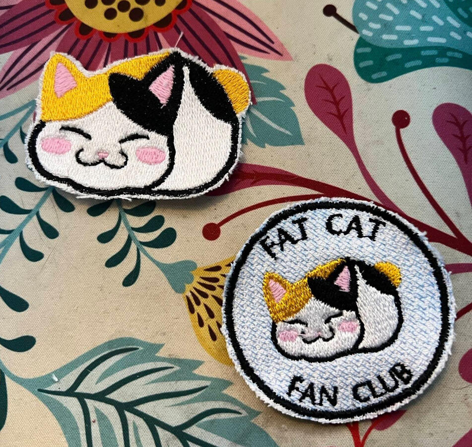 A pair of fat cat themed patches. Each shows the same cat, a piebald tabby in simple block art sitting, eyes contentedly closed and paws hidden underneath (oft called a 'loaf'). it has a half orange, half black head crest and back spots, with white belly a